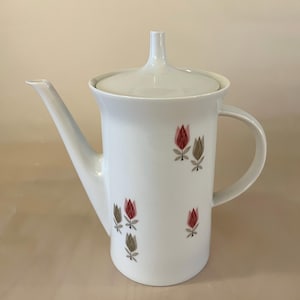 Peut inclure: Une cafetière en céramique blanche avec un couvercle et une poignée. La cafetière est décorée d'un motif floral avec des tulipes roses et brunes.