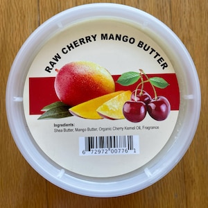 May include: A white plastic container with a red and white label that reads "RAW CHERRY MANGO BUTTER". The label also includes a picture of a mango, cherries, and the ingredients: Shea Butter, Mango Butter, Organic Cherry Kernel Oil, Fragrance. A barcode is printed on the bottom of the label.