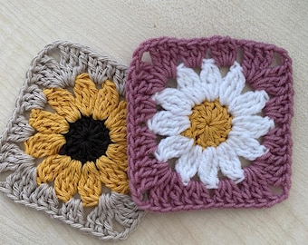 May include: Two crocheted squares, one with a yellow sunflower design and the other with a white daisy design. The sunflower square is on a beige background and the daisy square is on a pink background.