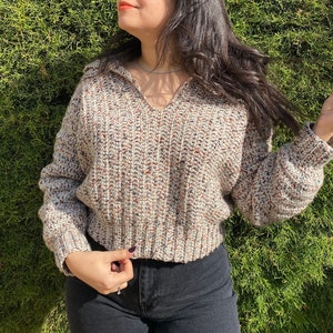 May include: A beige, brown, and white crocheted sweater with a v-neck and long sleeves.