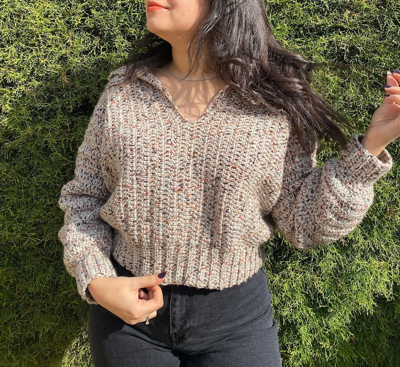 May include: A beige, brown, and white crocheted sweater with a v-neck and long sleeves.