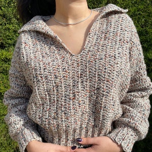 May include: A beige, brown, and black speckled crochet sweater with a v-neck and long sleeves.