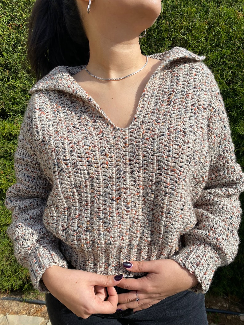 May include: A beige, brown, and black speckled crochet sweater with a v-neck and long sleeves.