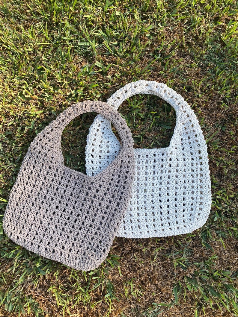 May include: Two crocheted bags, one in a light gray color and one in a darker gray color. The bags are made with a simple stitch pattern and have a wide, open top.