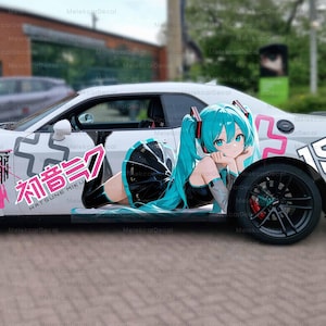 Puede incluir: Coche deportivo blanco con ruedas negras y detalles en rosa, con una gran ilustración de estilo anime de una chica con pelo turquesa. También se ve texto japonés y otros gráficos.