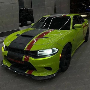 May include: A lime green Dodge Charger with a black hood and red racing stripes. The car has black rims and the text "SRTHERTZ" on the front bumper. The car is parked in a modern outdoor setting.