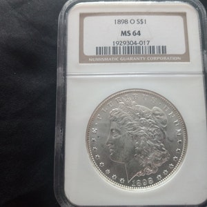 May include: A silver Morgan dollar coin graded MS 64 by the Numismatic Guaranty Corporation. The coin is dated 1898 'O' and has a serial number of 1929304-017.