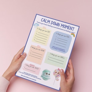 May include: A colourful "Calm Down Moment" worksheet with prompts for identifying feelings, held against a pink background. The worksheet includes sections for things to see, feel, hear, smell, and taste, with cartoon characters at the bottom.