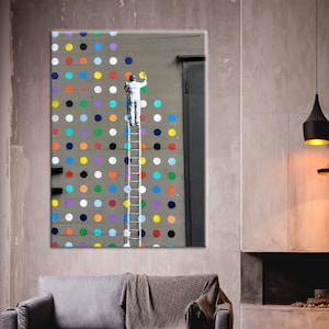 Op de afbeelding: Een groot ingelijst kunstwerk toont een figuur op een ladder die kleurrijke stippen op een grijze muur schildert. De kamer heeft een grijze bank, een kerstboom en moderne zwarte hanglampen.