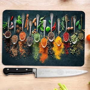 Puede incluir: Una tabla de cortar rectangular con un fondo oscuro presenta una variedad de especias en cucharas antiguas. Debajo hay un cuchillo de chef grande con mango negro y hoja plateada. Verduras y frutas frescas en el fondo.