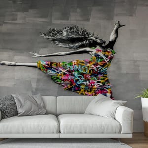 May include: A mural of a dancing figure with a dress covered in colorful graffiti art. The artwork is on a gray wall above a white sofa with gray pillows. A modern interior design with a plant in a white pot is also visible.