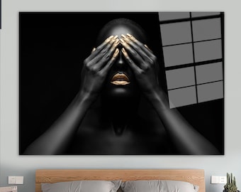 May include: A person with black skin and gold painted fingernails and lips covers their eyes with their hands. The background is black with a window pane.