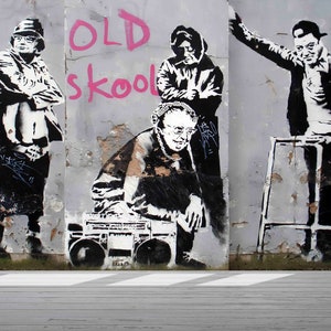 May include: Black and white stencil art on a gray wall depicting three people. The text "OLD skool" is written in pink paint. One person is holding a boombox, another is holding a walking stick, and the third person is standing with their arms crossed.