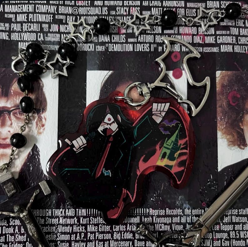 以下が含まれることがあります： 黒と赤のアニメスタイルのキャラクターキーホルダーで、赤と黄色の炎のデザインが施されています。キーホルダーは、銀色のチェーンに銀色の星形のチャームが付いています。