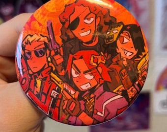 May include: A circular pin-back button featuring a vibrant, stylized illustration of four characters in an action-oriented scene. The artwork uses a warm color palette of oranges, reds, and purples, depicting figures with weapons against a bright background.