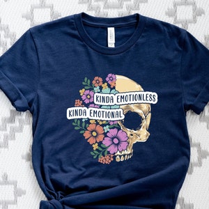 Puede incluir: Una camiseta azul marino con un gr&aacute;fico de calavera. La calavera est&aacute; medio cubierta de flores y tiene el texto "Kinda Emotional" y "Kinda Emotionless" en ella.