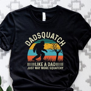 May include: Black t-shirt with a vintage-style graphic of a Bigfoot walking in front of a sunset. The text reads "Dadsquatch Like a Dad Just Way More Squatchy".