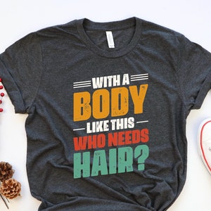 May include: A dark gray t-shirt with a vintage-style graphic that reads "With a Body Like This Who Needs Hair?" The graphic features a red, orange, yellow, and green color scheme.
