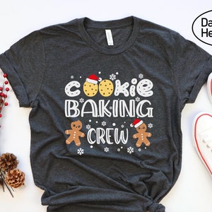 May include: Dark grey heather t-shirt with the text "Cookie Baking Crew" and a gingerbread man and cookie graphic.