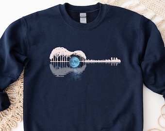 Op de afbeelding: Een donkerblauw sweatshirt met een witte afbeelding van een gitaarsilhouet met een volle maan in het klankgat. De maan is blauw en de bomen zijn wit.