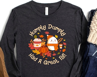 May include: A dark gray long-sleeve shirt with a white and orange graphic of a smiling egg with a scarf and a pumpkin. The text "Humpty Dumpty Had A Great Fall" is printed in a circle around the graphic.