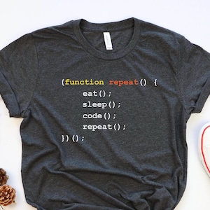 May include: A dark gray t-shirt with white text that reads: (function repeat() { eat(); sleep(); code(); repeat(); })();