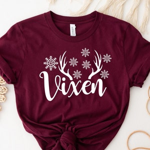 May include: Burgundy t-shirt with white text that says "Vixen" and a white snowflake and reindeer antler design.