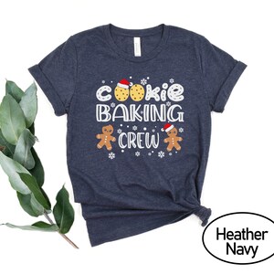 May include: A navy blue t-shirt with the text "Cookie Baking Crew" in white. The design includes gingerbread men and cookies.