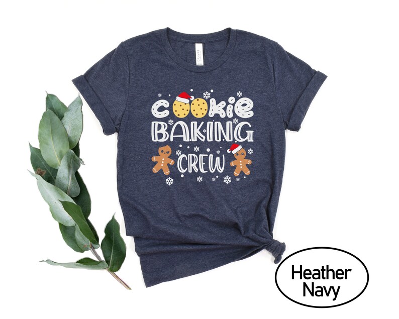 May include: A navy blue t-shirt with the text "Cookie Baking Crew" in white. The design includes gingerbread men and cookies.