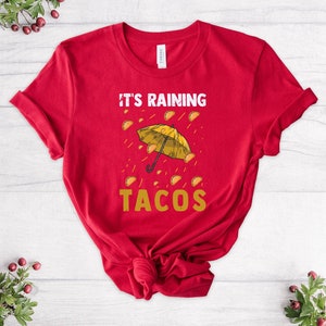 Peut inclure: T-shirt rouge avec un parapluie jaune et le texte "Il pleut des tacos".
