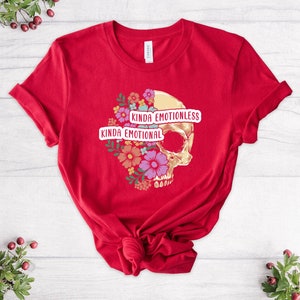 Puede incluir: Camiseta roja con un gr&aacute;fico de calavera y dise&ntilde;o floral. El texto "Kinda Emotional" y "Kinda Emotionless" est&aacute; impreso en la camiseta.