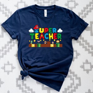 Puede incluir: Una camiseta azul marino con un gr&aacute;fico de un personaje de Super Mario Bros. y el texto "SUPER TEACHER".