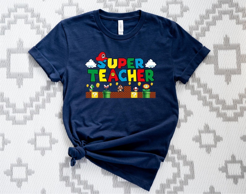 Puede incluir: Una camiseta azul marino con un gr&aacute;fico de un personaje de Super Mario Bros. y el texto "SUPER TEACHER".