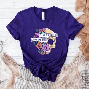 Puede incluir: Camiseta morada con un gr&aacute;fico de calavera y el texto "Kinda Emotionless Kinda Emotional".