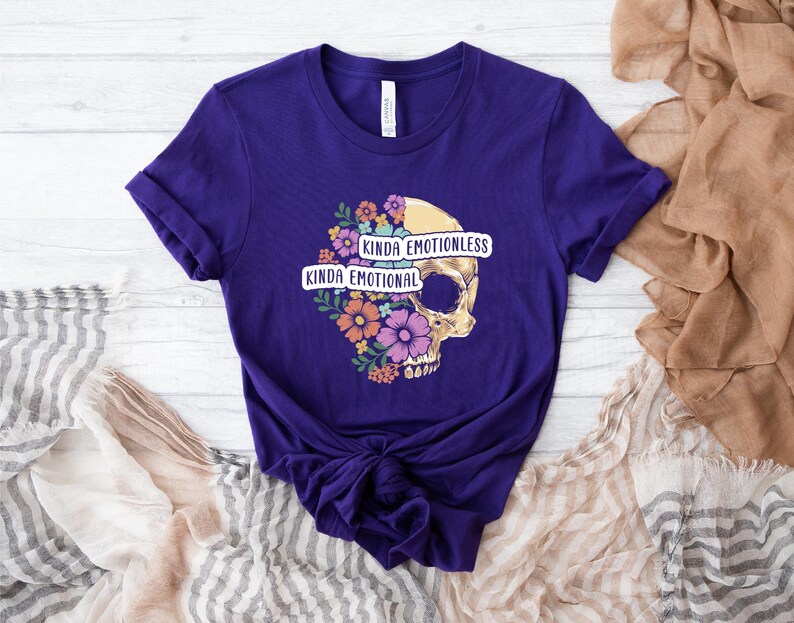 Puede incluir: Camiseta morada con un gr&aacute;fico de calavera y el texto "Kinda Emotionless Kinda Emotional".