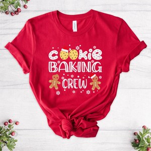 May include: Red t-shirt with a white graphic that says "Cookie Baking Crew" with gingerbread men on either side of the text.