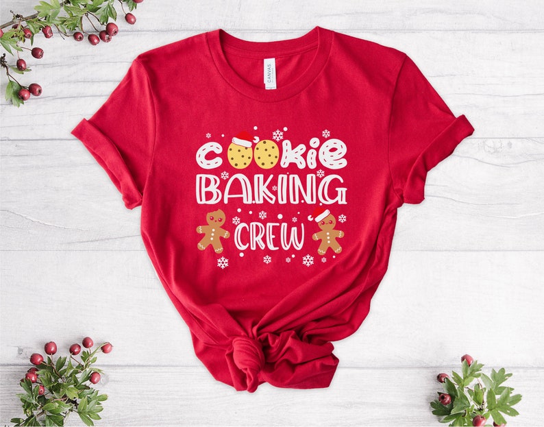 May include: Red t-shirt with a white graphic that says "Cookie Baking Crew" with gingerbread men on either side of the text.