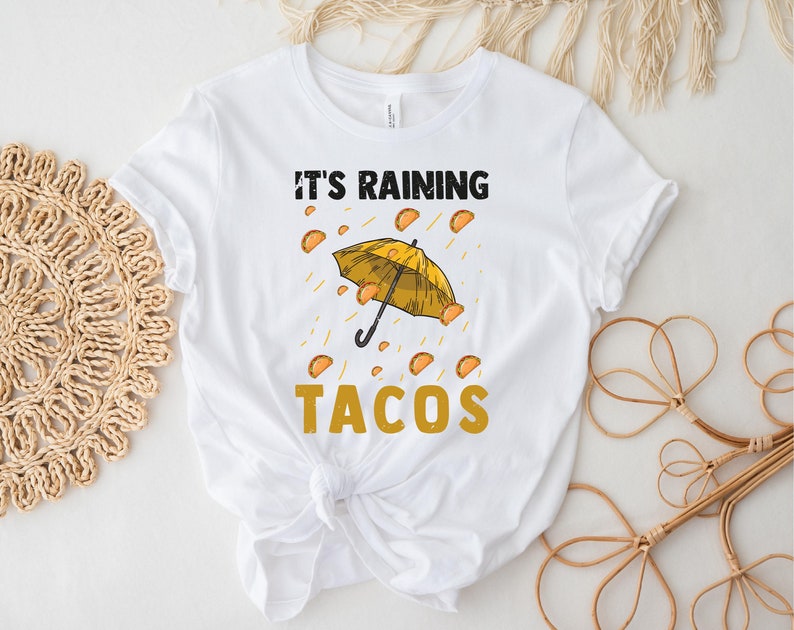 Peut inclure: T-shirt blanc avec un parapluie jaune et le texte "Il pleut des tacos" imprim&eacute; dessus.