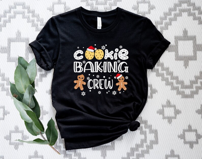 May include: Black t-shirt with a white graphic that says "Cookie Baking Crew" with gingerbread men and cookies wearing Santa hats.