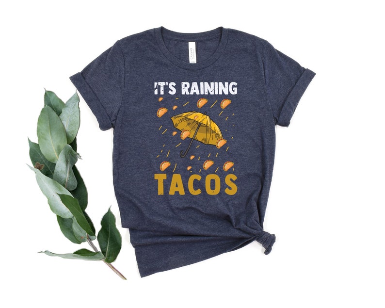 Peut inclure: Un t-shirt bleu marine avec un imprim&eacute; blanc d'un parapluie jaune avec des tacos qui tombent du ciel. Le texte "It's raining tacos" est imprim&eacute; sous le parapluie.