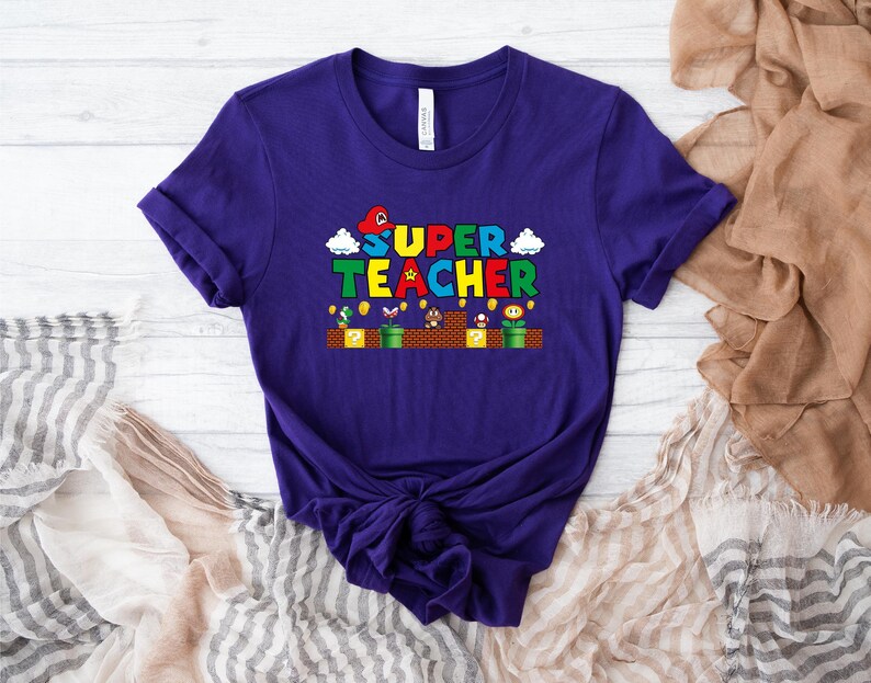 Puede incluir: Camiseta morada con un gr&aacute;fico de un personaje de videojuego y el texto "SUPER TEACHER".