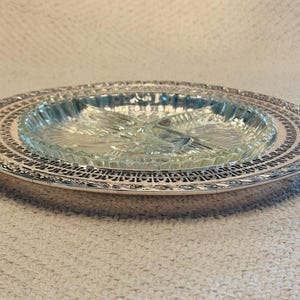 May include: An oval serving dish with a clear glass insert and a silver-colored metal filigree border. The glass insert is divided into sections. The dish is designed for serving appetizers or snacks.