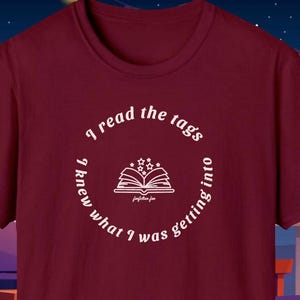 Peut inclure: T-shirt bordeaux avec un motif blanc. Le motif représente un livre ouvert avec des étoiles et le texte "I read the tags, I knew what I was getting into" dans un design circulaire. Le texte "fanfiction fan" est également inclus.