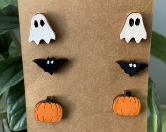 May include: A set of six Halloween-themed earrings featuring a ghost, bat, and pumpkin design. The earrings are made of wood and painted in white, black, and orange.