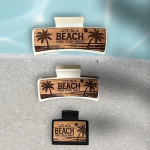 May include: Three hair clips with a wood grain design and the text "Life is a Beach Find Your Wave". The clips are white, black, and white.