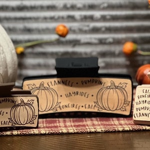 May include: Three brown and black hair clips with a fall theme. Each clip has a different design with a pumpkin and text that reads "Flannels, Pumpkins, Hayrides, Bonfires, Fall".
