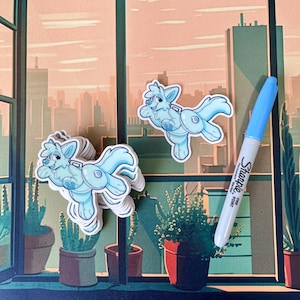 Op de afbeelding: Een stapel lichtblauwe wolf stickers met een witte omtrek. De stickers liggen op een tafel met een raam op de achtergrond. Het raam heeft uitzicht op een skyline van de stad. Er ligt een blauwe Sharpie fijne punt stift op de tafel.