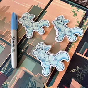 Op de afbeelding: Drie blauwe en witte cartoon-hondenstickers met een reddingsvest op hun rug. De stickers zijn op een bruine en oranje achtergrond.