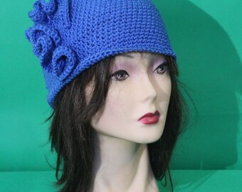 May include: A blue crocheted hat with a flower detail. The hat is on a mannequin head with brown hair.
