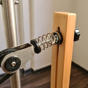 Peut inclure: Gros plan d'un système de poulie en bois avec un ressort métallique et un bouton noir. Une corde noire est passée dans la poulie.